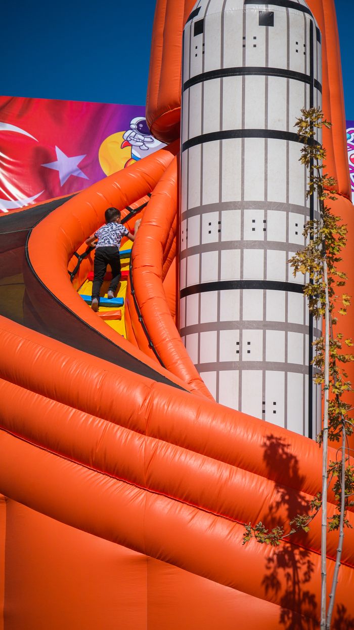 our-vission A child climbs up a colorful, inflatable space-themed slide outdoors on a sunny day.