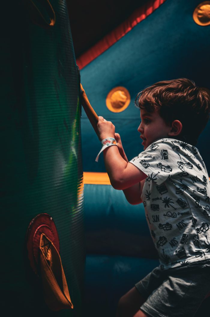 my-work-img Young boy climbing on colorful inflatable surface indoors, focused and determined.