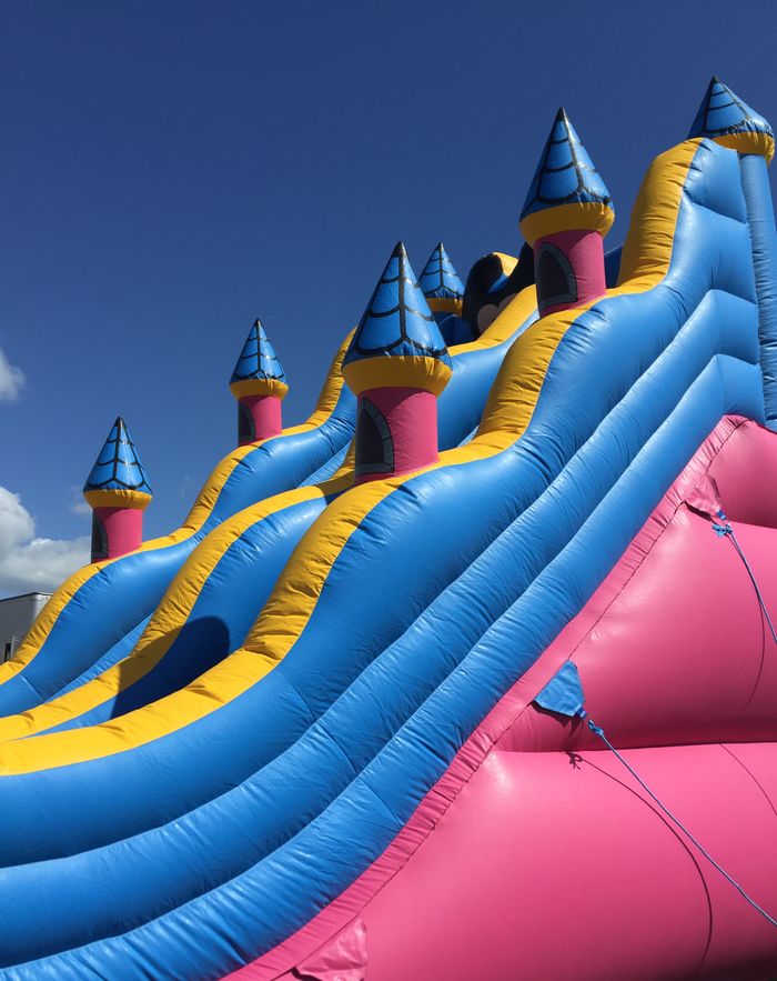 service-02 Bright inflatable slide with colorful turrets against a clear blue sky. Fun and playful atmosphere.